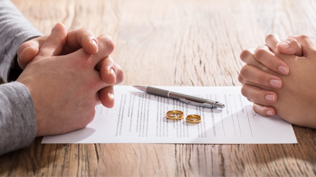 divorcing couples folded hands across from each other on top of divorce papers 1024x576